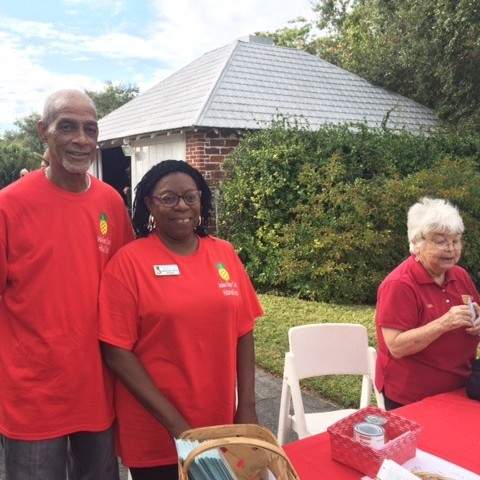 Man and two ladies standing at red table